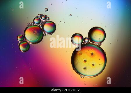 two groups of oil droplets float over a water surface illuminated in different colors Stock Photo