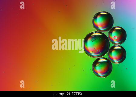 five colored oil droplets drift over a brightly lit water surface, close-up Stock Photo