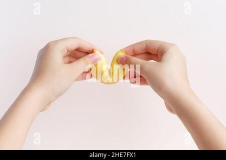 Girl's hands open Fortune cookie on a pastel pink background. Chinese tradition Stock Photo