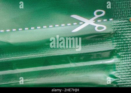 Macro shot of white scissors symbol and dotted cutting line on the plastic food packaging. For cutting along the line, cut above the rest metaphor. Stock Photo