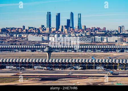Madrid, Spain - December 31, 2021: Control tower of Adolfo Suarez Madrid-Barajas airport against cityscape with Cuatro Torres Business Area skyscraper Stock Photo
