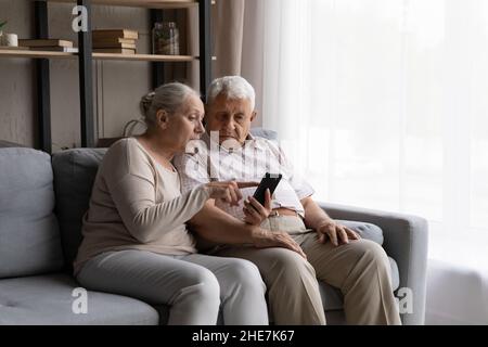 Happy older generation retired family couple learning using smartphone. Stock Photo