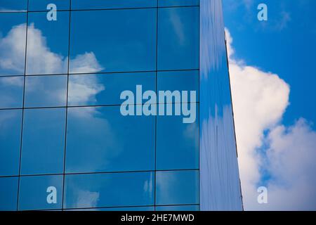 Reflections of blue sky and white clouds on the glass of the windows of an office building. Stock Photo