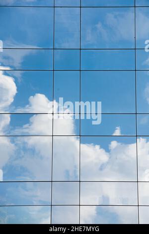 Reflections of blue sky and white clouds on the glass of the windows of an office building. Stock Photo