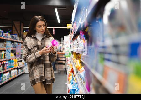 Woman reading the label on the packaging of laundry powder in the household chemicals department of the supermarket Stock Photo