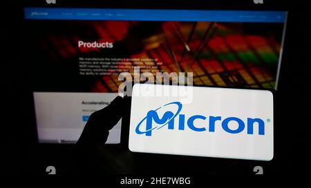 Person holding smartphone with logo of US semiconductor company Micron Technology Inc. on screen in front of website. Focus on phone display. Stock Photo