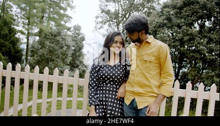 Shallow focus of a young Indian couple happily having a date at a park beside a wooden fence Stock Photo