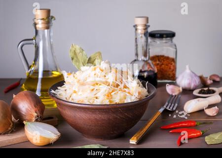 Close-up of sauerkraut fermented cabbage in ceramic sauerkraut bowl on table with spices and ingredients. Healthy healthy food. Russian kitchen. Selec Stock Photo