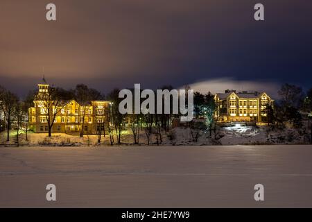 Illuminated Linnunlaulu villas viewed over frozen Töölönlahti Bay after dark in Helsinki, Finland Stock Photo