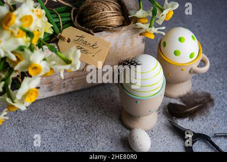 Easter floral card concept with daffodil flowers in wooden box with colored eggs on concrete background Stock Photo