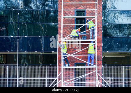four workers in uniform and safety protective equipment on the scaffolding clean the brick facade of the building Stock Photo