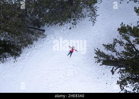 Drone aerial of woman wearing warm clothing lie down at snow in winter. Troodos cyprus Stock Photo