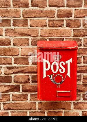 Traditional old bright red metal post box with word and picture of horn on front attached to facade of house, old brick wall of home. Postal service p Stock Photo