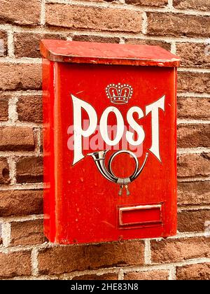 Traditional old bright red metal post box with word and picture of horn on front attached to facade of house, old brick wall of home. Postal service p Stock Photo