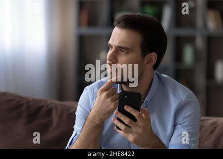 Head shot thoughtful serious man looking in distance, holding smartphone Stock Photo