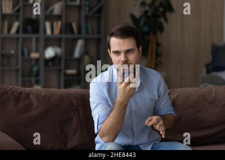 Serious man recording audio message on smartphone, sitting on couch Stock Photo