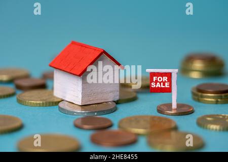 Tiny house on money and a for sale sign - Housing market, real estate, property investment, saving money, habitation cost concept Stock Photo