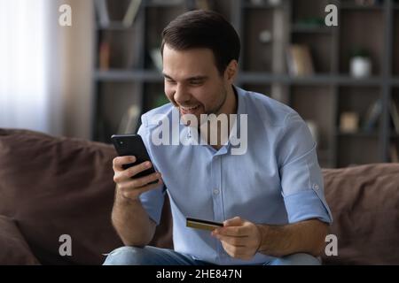 Excited man paying by gold credit card online, using smartphone Stock Photo