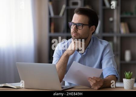 Thoughtful serious businessman in glasses touching chin, holding document Stock Photo