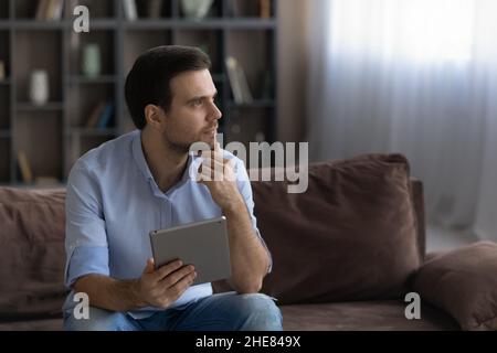 Thoughtful man holding tablet, touching chin, looking in distance Stock Photo