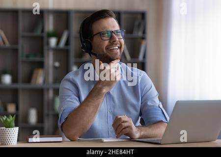 Laughing man in headset and glasses using laptop, taking notes Stock Photo