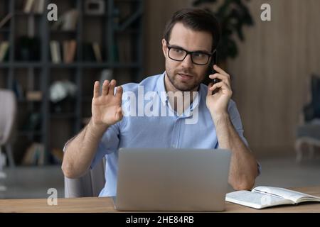 Confident serious businessman in glasses talking on phone, using laptop Stock Photo