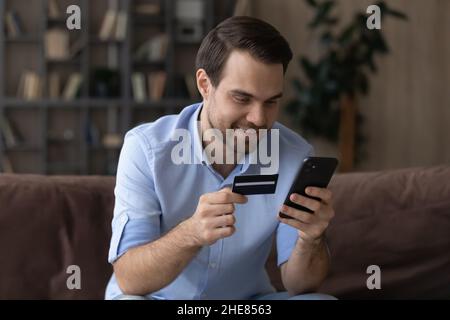 Smiling man holding smartphone and credit card, paying online Stock Photo
