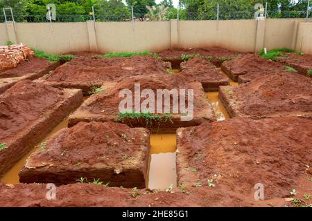 Building foundation that was dug in sand soil. The dug out soil was placed in mounts around the trenches . Trenches filled with muddy water Stock Photo