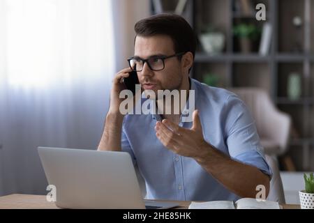 Confident businessman in glasses talking on phone, sitting at desk Stock Photo