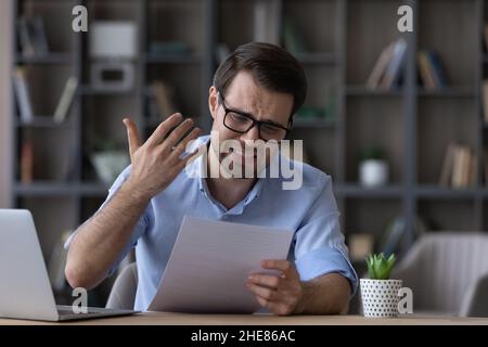 Unhappy frustrated man in glasses reading bad news in letter Stock Photo