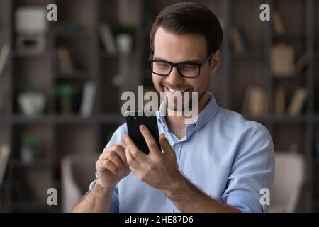 Head shot smiling man wearing glasses using smartphone, chatting online Stock Photo