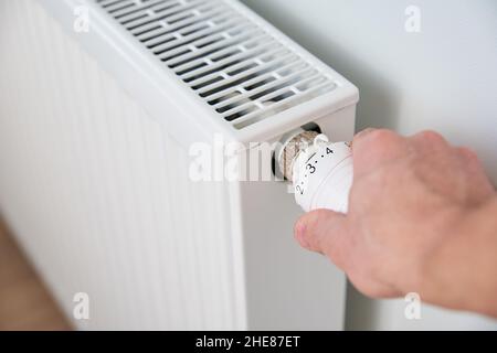 Hand adjusting temperature on heating radiator thermostat, Turning heat radiator knob to control heat in home Stock Photo