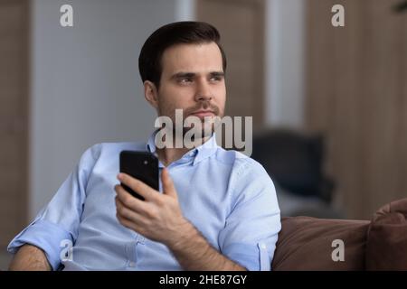 Head shot thoughtful man holding smartphone, looking in distance Stock Photo