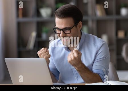 Head shot excited businessman in glasses celebrating success, using laptop Stock Photo