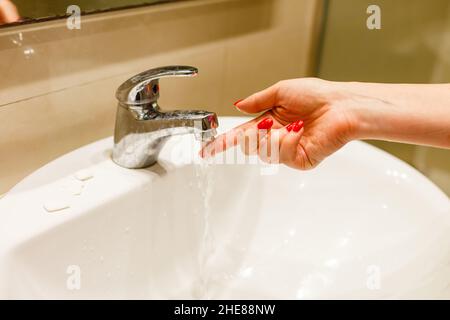 Woman taking a bath at home checking temperature touching running water with hand. Closeup on fingers under hot water out of a faucet of a sink or Stock Photo