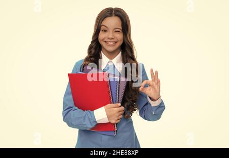 winking child long curly hair hold school workbook isolated on white show ok gesture, high school Stock Photo