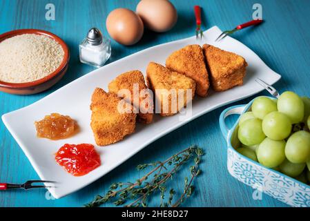 Fried Camembert cheese in portions with breadcrumbs, eggs,marmalade and grapes. Stock Photo