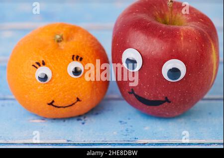 Tangerine And Red Apple With Funny Faces On Blue Background Stock Photo