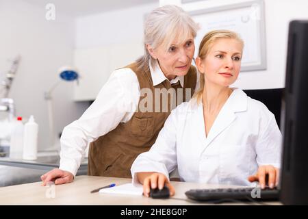 Interested elderly female client with cosmetologist looking at computer screen Stock Photo