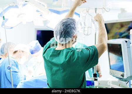 Moscow. Russia. December 24, 2021. Rear view of a male doctor in medical uniform in the operating room during surgery. The doctor is replacing the saline dropper bag. Stock Photo