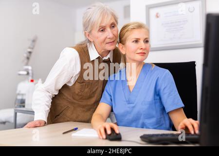 Interested elderly female client with cosmetologist looking at computer screen Stock Photo