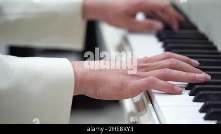 Close-up hands of a young man in a white jacket play music on the piano.Classical music, concert, performance.Music lessons on the piano, keyboard ins