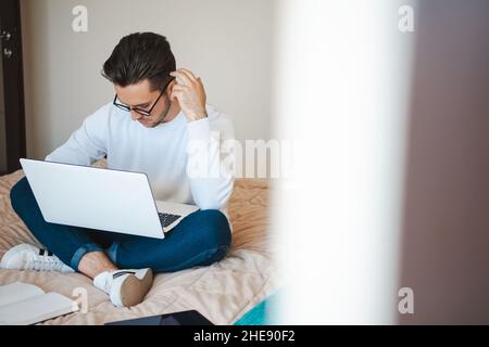 Businessman working and using laptop while sitting with cross-legged on bed. Internet technology. Online communication. Stock Photo
