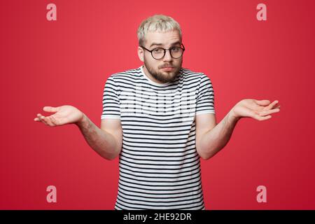 Front view of a caucasian man in eyeglasses shrugging shoulders on pink studio background. Guy portrait lifestyle. Fashionable portrait. Stock Photo