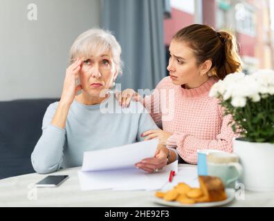 Worried elderly woman with adult daughter checking utility bills Stock Photo