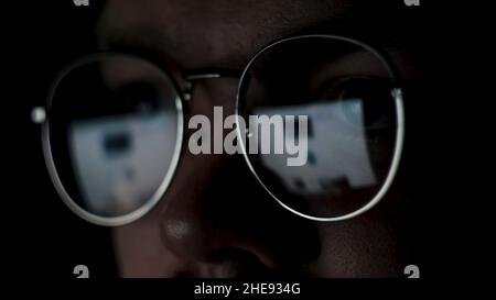 Close up of the eyes of a man with glasses at the computer isolated on black background. The reflection of the screen in the glasses of a genius or ne Stock Photo