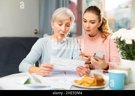Elderly woman with adult daughter using smartphone and checking utility bills Stock Photo