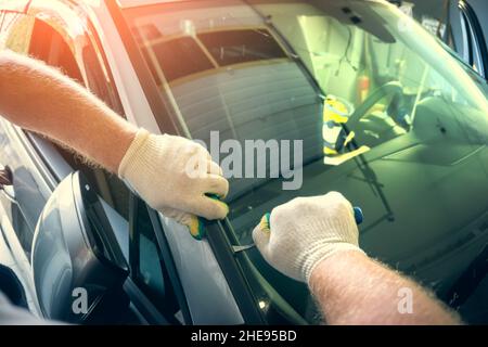 Service worker dismantle broken glass windscreen or windshield before installing new one on car in auto station garage. Stock Photo