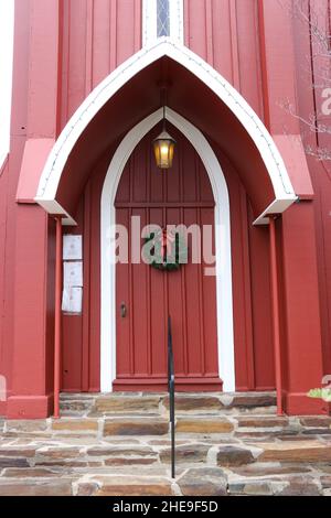 Festive Christmas wreath on a red wooden church door welcomes the Advent season. A golden light hangs over the door. Stock Photo