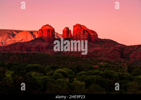 Rock formations surrounding Sedona, Arizona, US. Prominent orange buttes, with contrasting green plants during orange sunset. Stock Photo